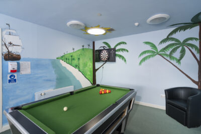 A pool table and dart board in a room with a chair.