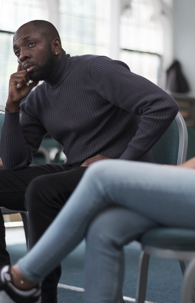 Black man sitting with hand to his chin.