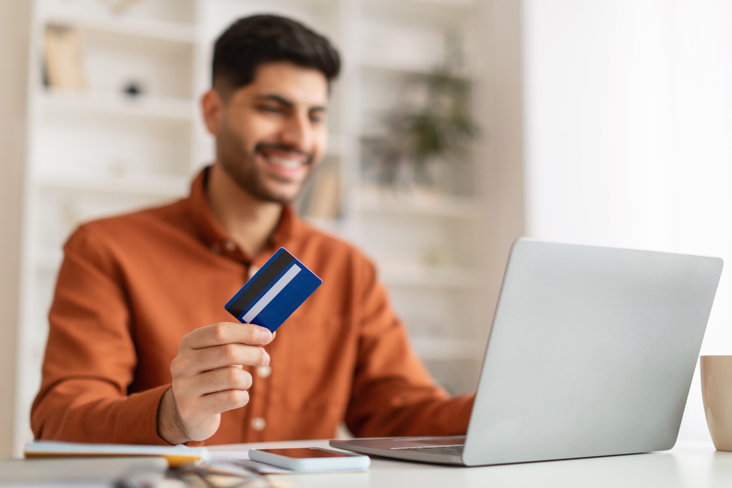 A man sitting, looking at a laptop with a credit card.