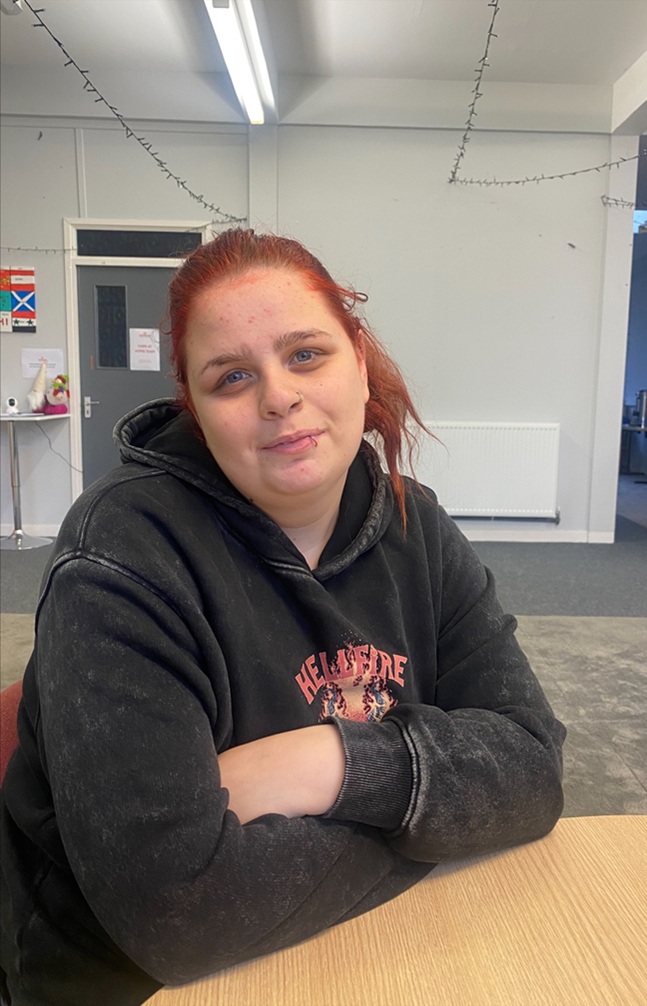 Woman with red hair pulled back wearing a black hoodie and arms crossed.