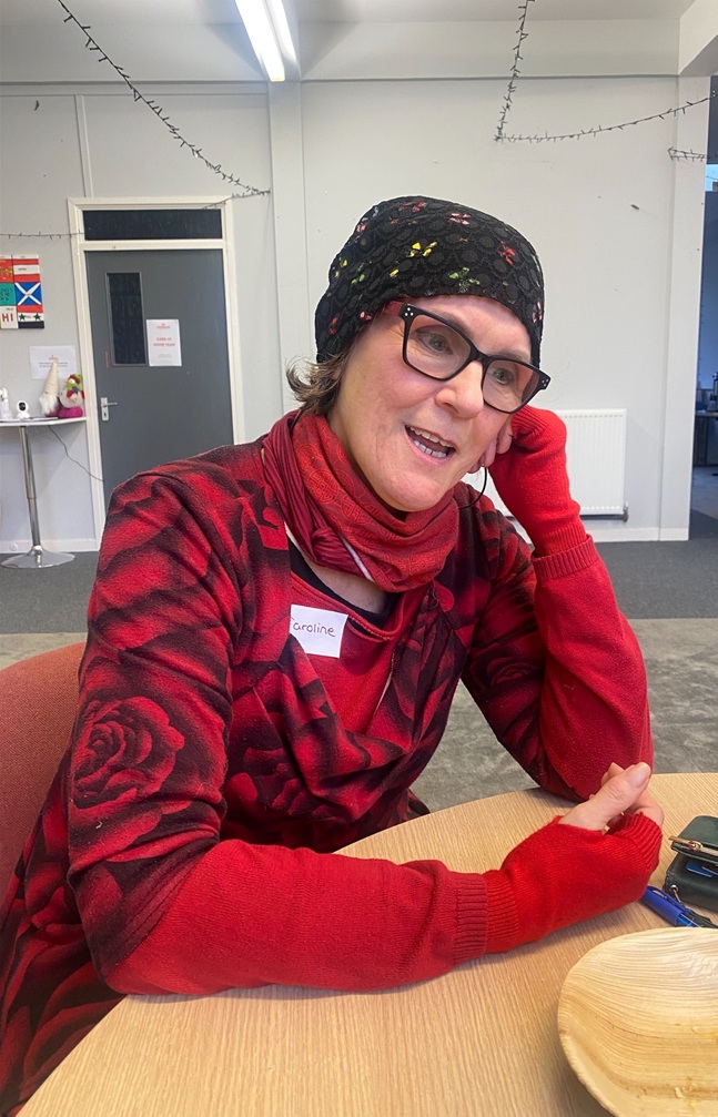 A woman with a hat and glasses, sitting at a table smiling down.