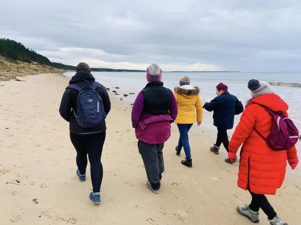 Group of people walking on a beach with coats.