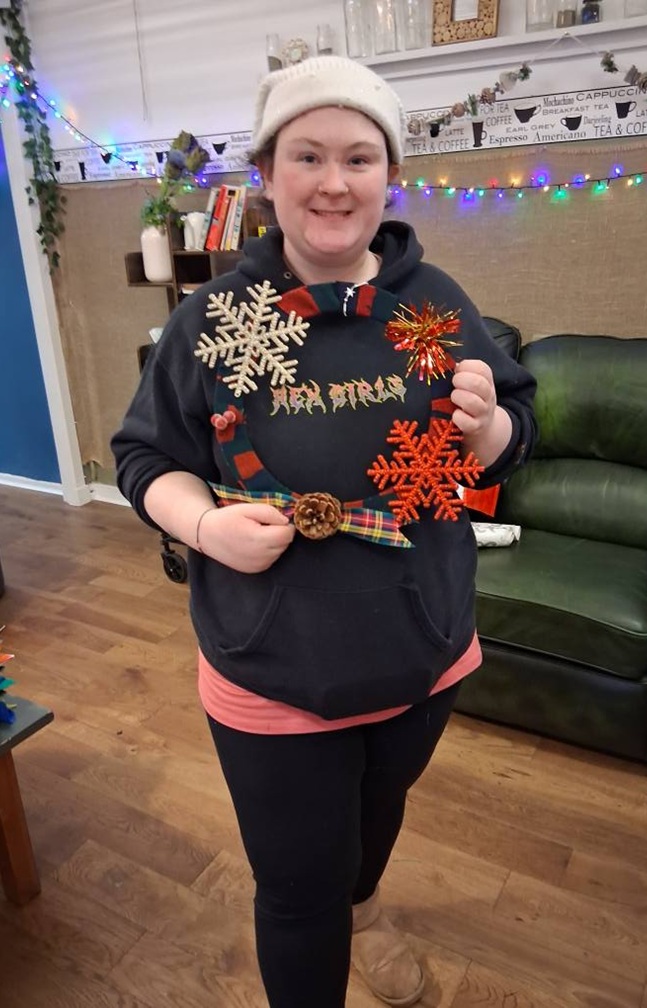 Young woman standing with a hat on and carrying Christmas decorations.