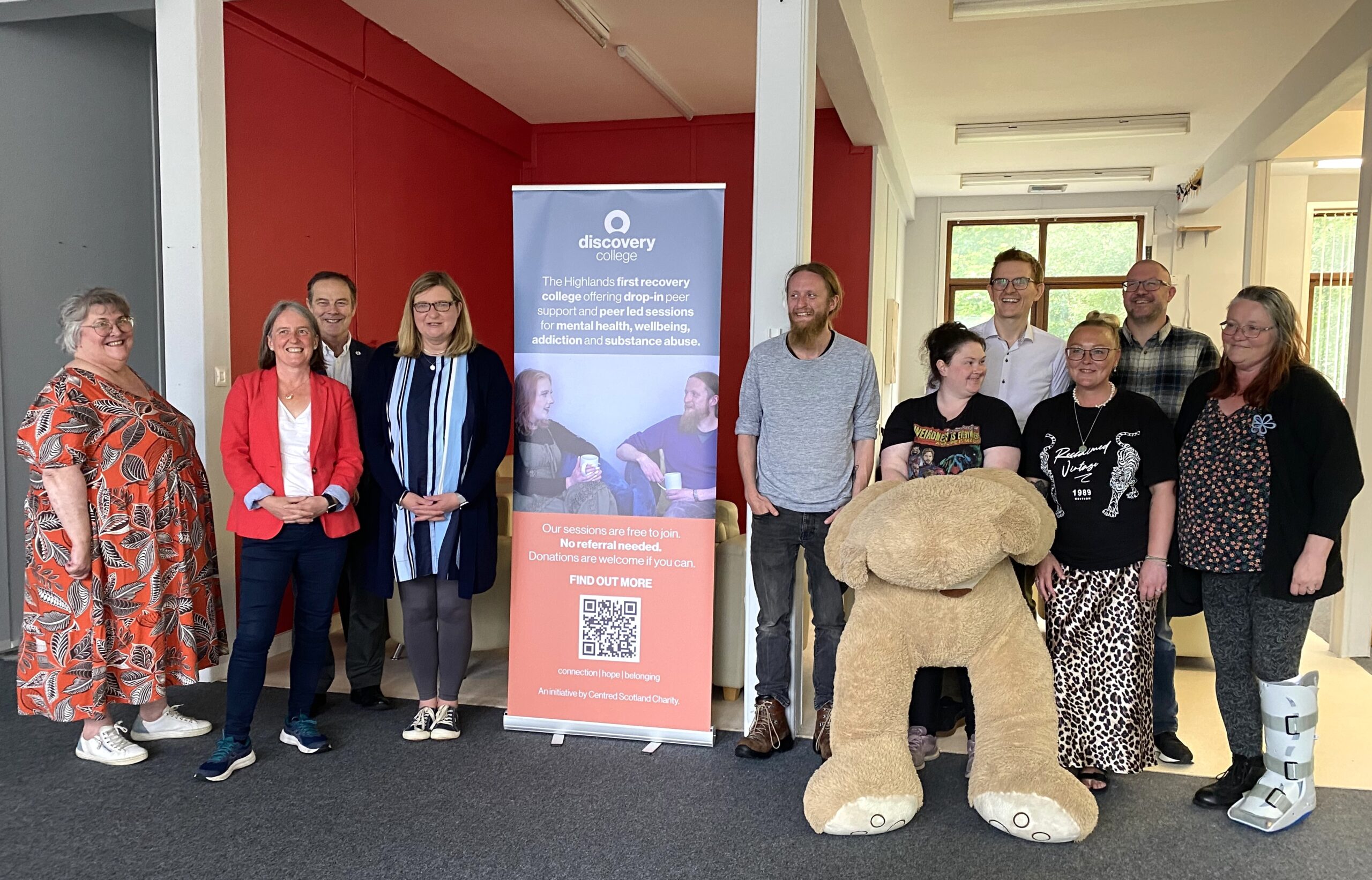 Group of people launching the Discovery College in Wick with banner and large teddy.