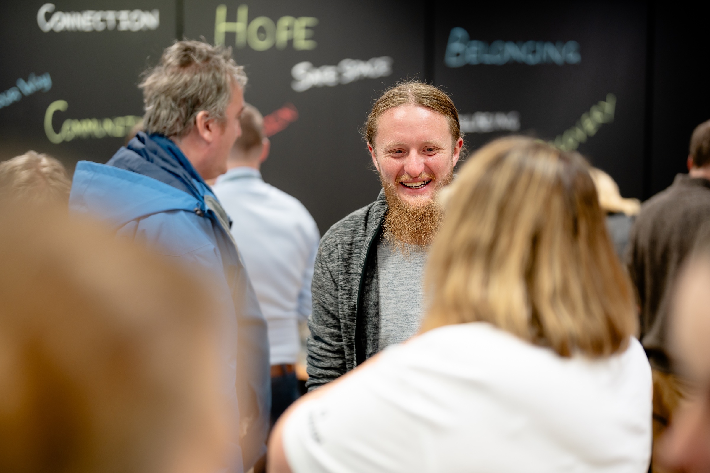 Man with beard smiling with other people with their backs to the camera