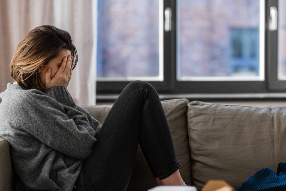 Woman lying on couch with hands over her face in despair.