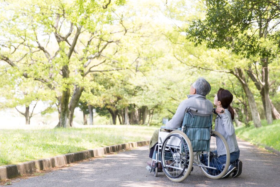 Female carer with elderly man in wheelchair outside in a park