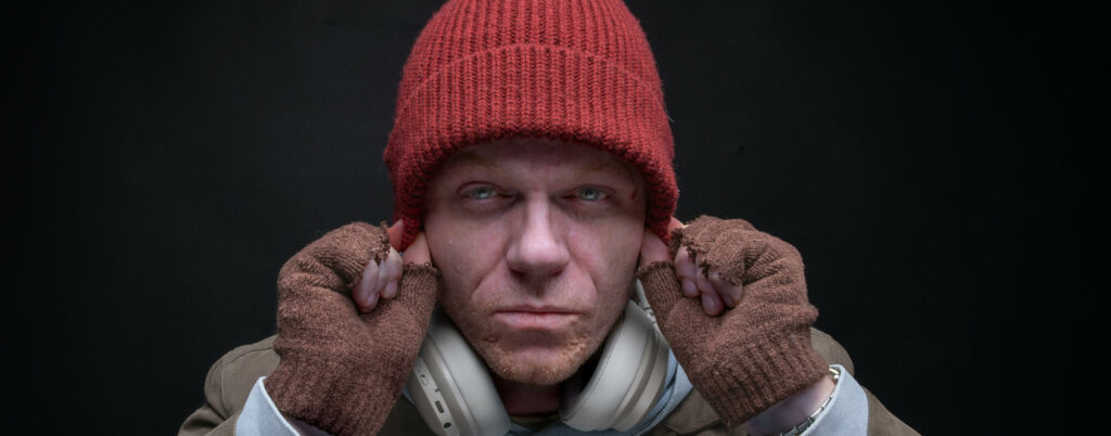 Picture of a man with a beanie hat, holding his ears and looking at the camera