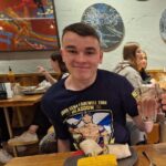 Photo of a young man smiling with a beer sitting at a table