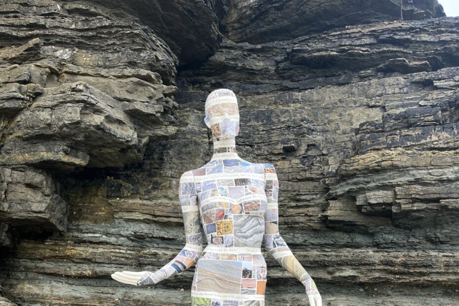 Female mannequin covered in text and pictures next to a rock