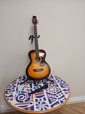Picture of a guitar standing upright on a mosaic table with microphone