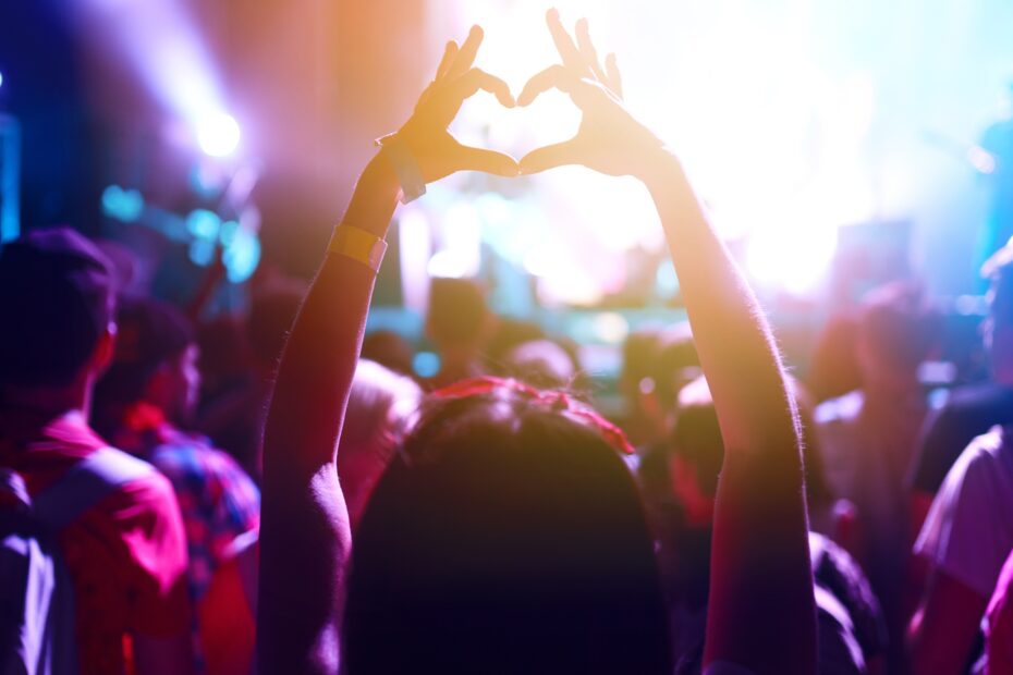 People watching a music event with someone making a heart symbol with their hands