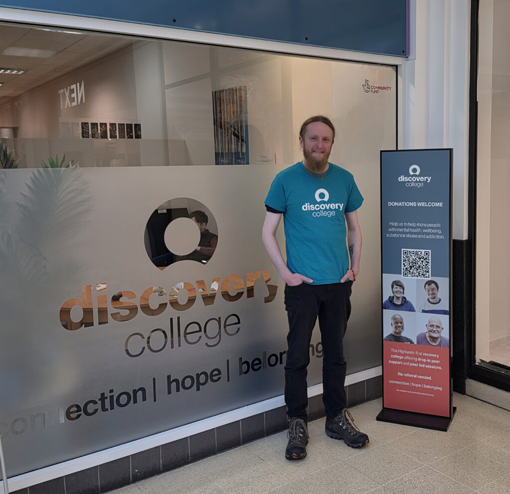 Man with red hair and beard standing in front of the Discovery College