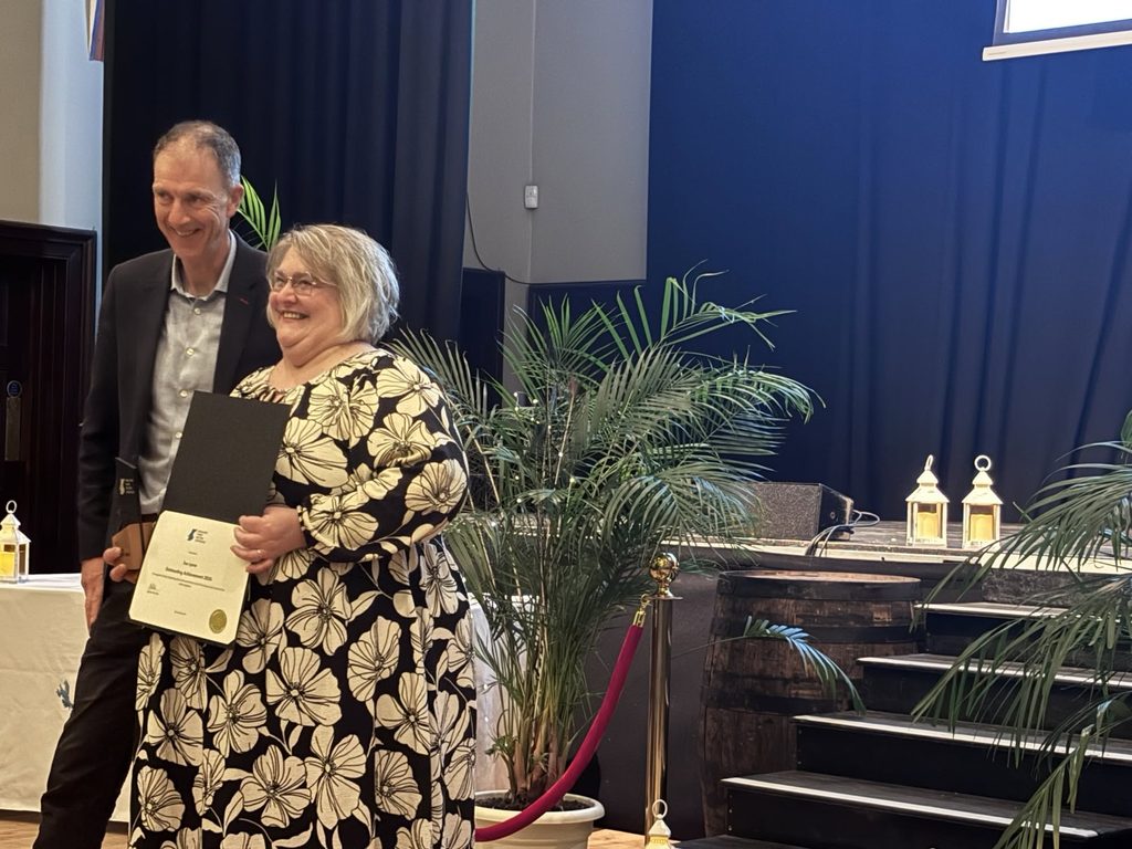 A woman in a floral dress smiling whilst receiving an award from a man